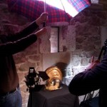 A WW1 helmet is photographed while an assistant shades the camera from the sun with an umbrella